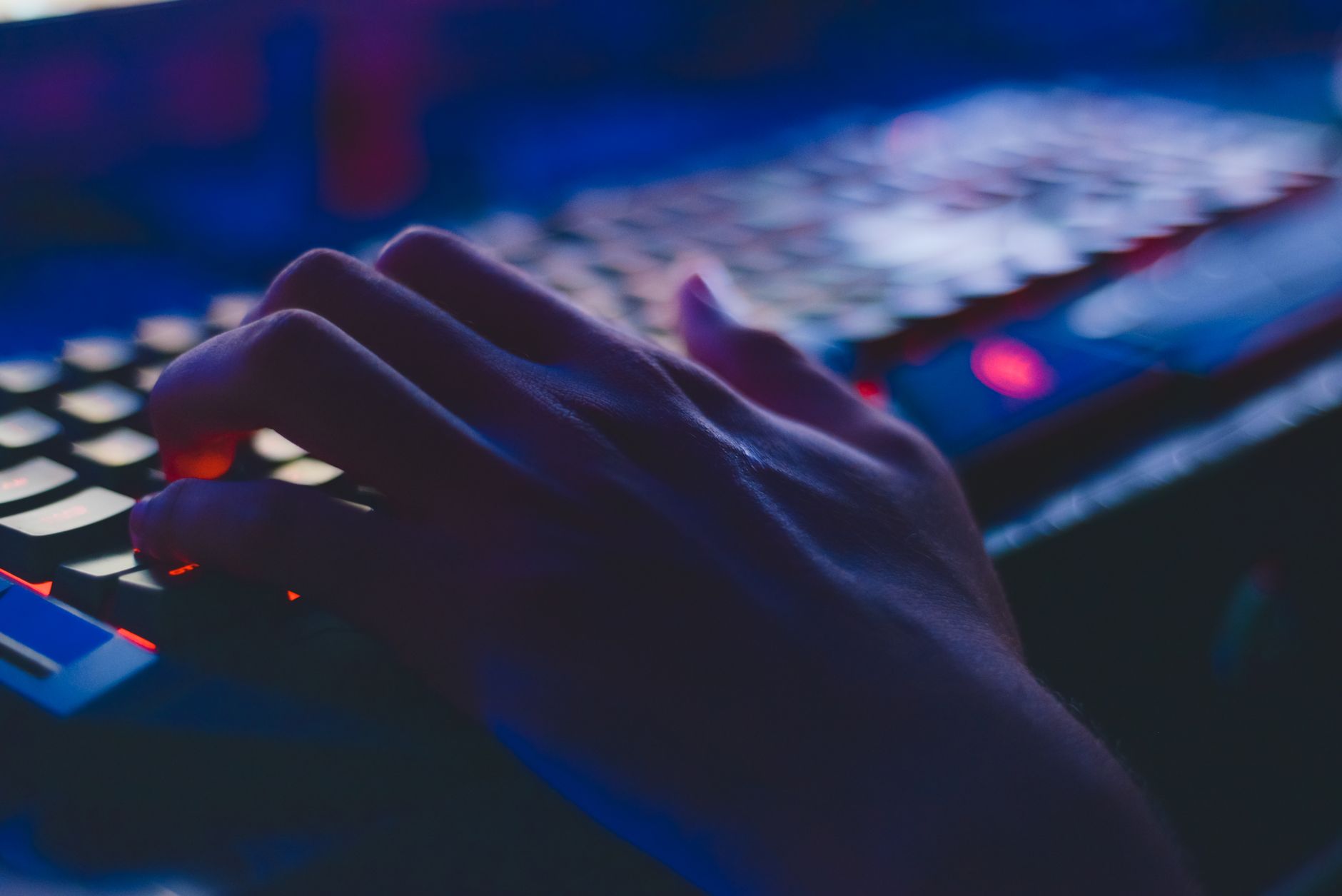 close up of fingers typing on a metallic laptop keyboard in a dark room