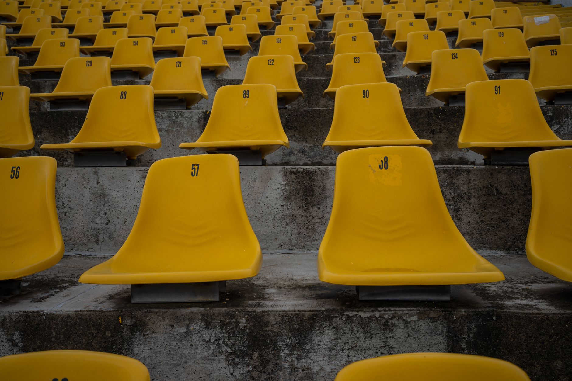 brutalist concrete stadium roof casting dramatic shadows on empty seats