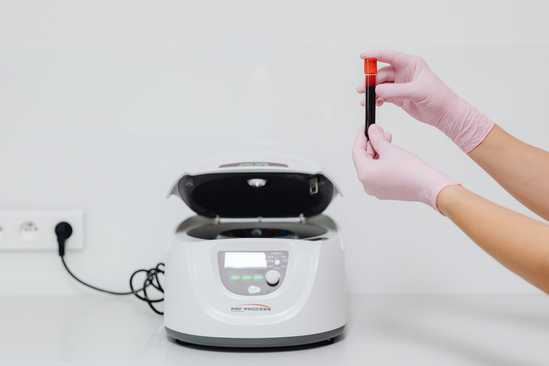 a scientist holding a small vial of dark red blood next to a centrifuge
